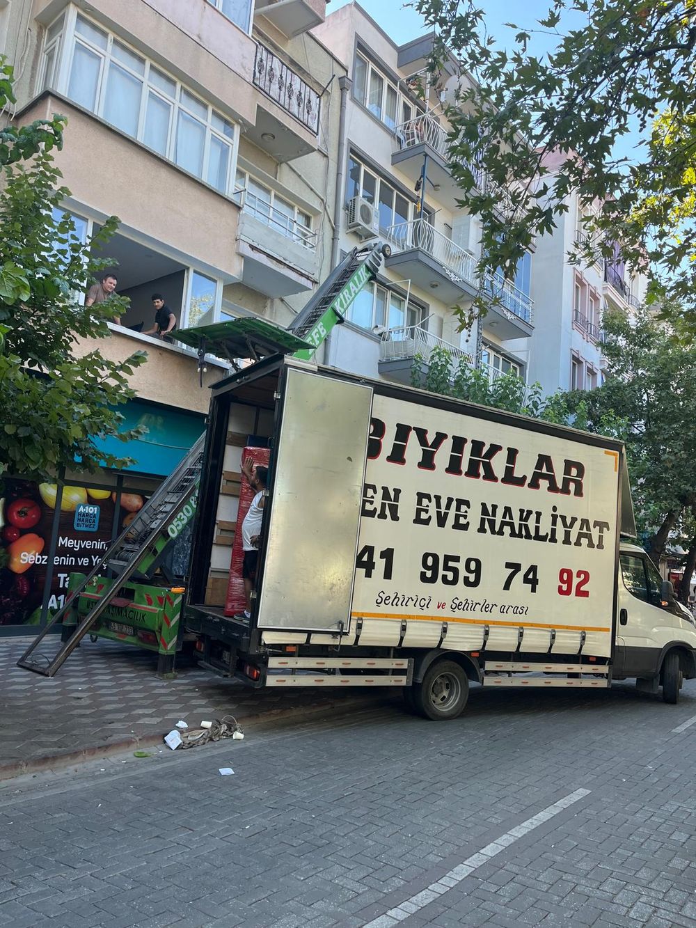 Bıyıklar Nakliyat kamyonu, kırmızı streç filmle sarılı eşyalar ve vinçle balkondan taşıma